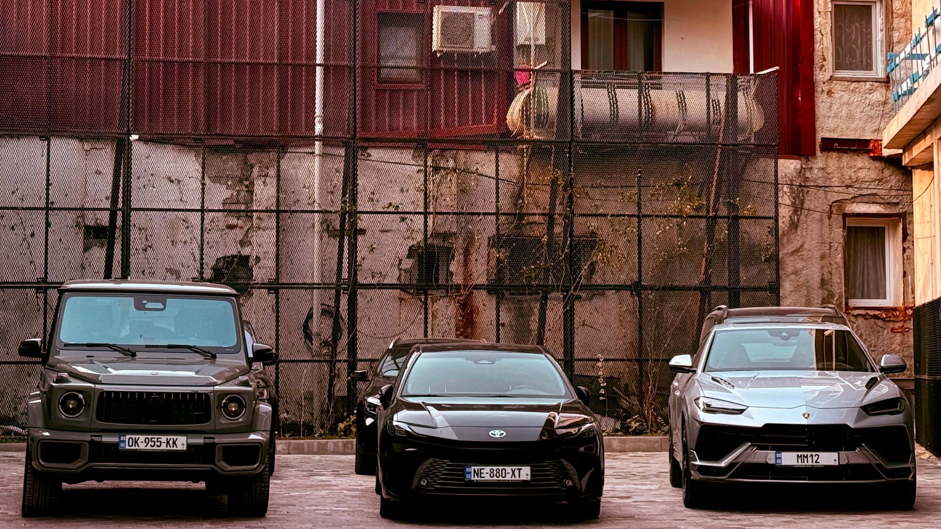Three cars parked in an urban area with a red building and decorative architecture in the background.