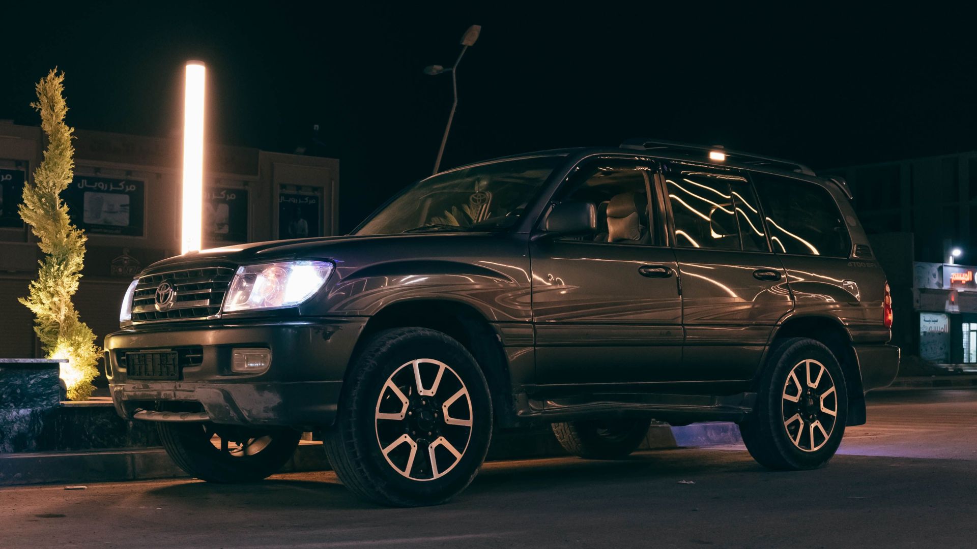 A dark SUV parked under streetlights on a city street at night, showcasing urban aesthetics.