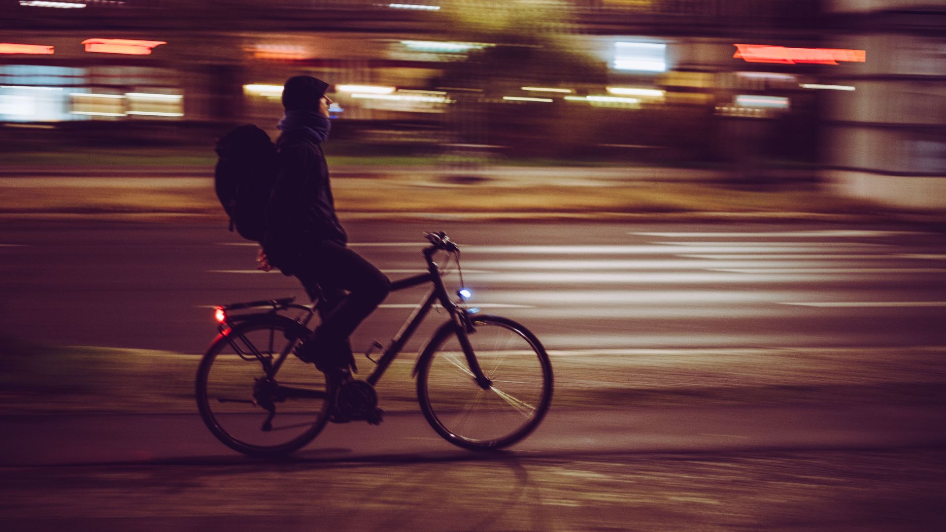 Blurry image of a cyclist moving swiftly through illuminated city streets at night.