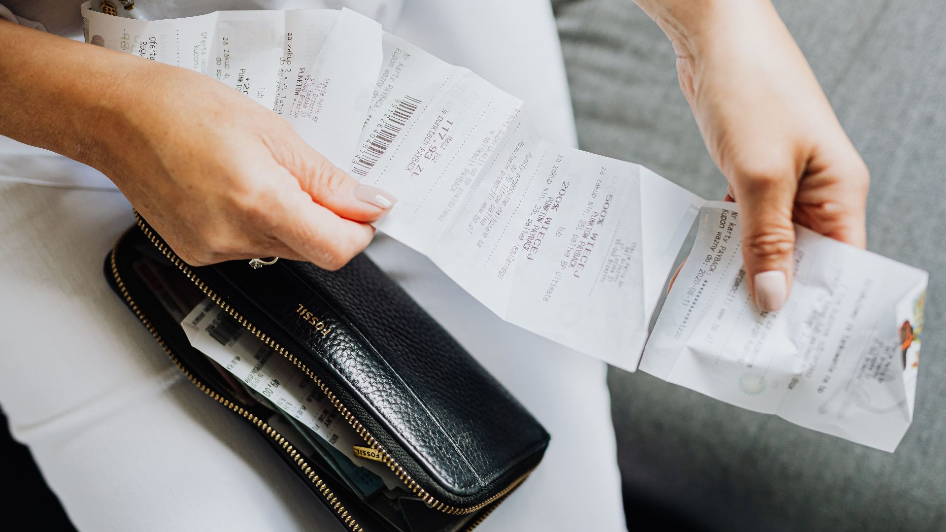 Close-up of a woman's hands managing multiple receipts taken from a black wallet.