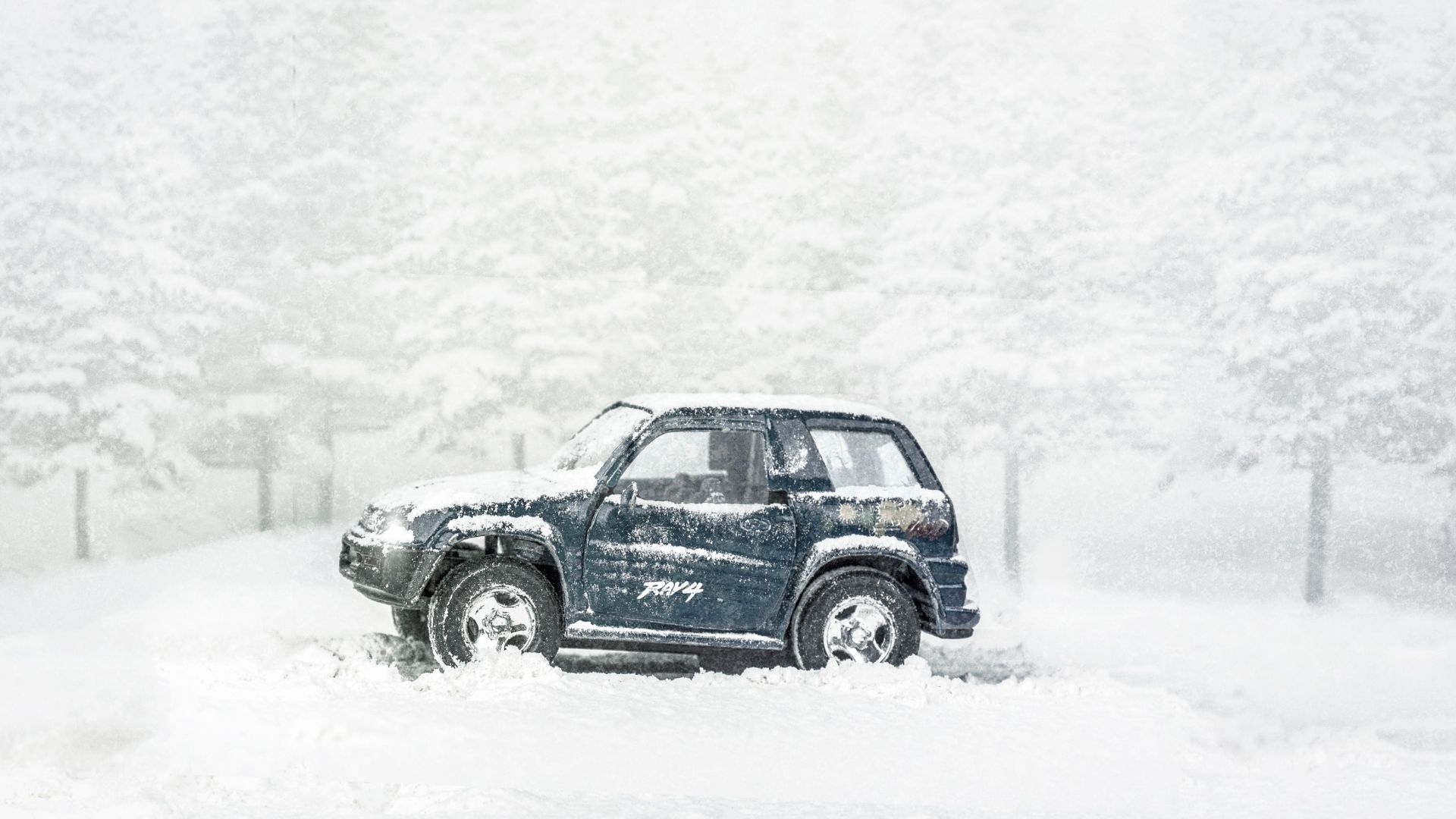 A Toyota RAV4 navigates through a heavy snowstorm and icy winter landscape.