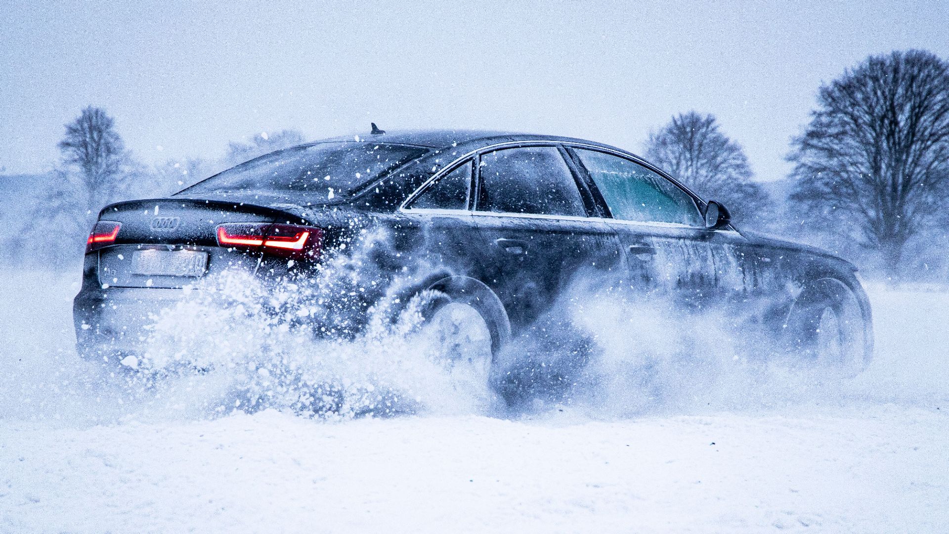 A sleek black car powers through snow, creating a dynamic winter scene with swirling snowflakes.