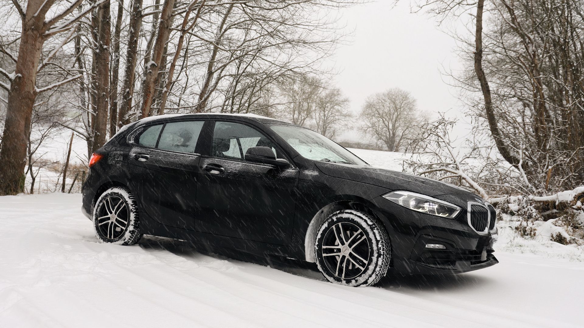 A black car driving through a snowy forest landscape, embodying winter weather's beauty.