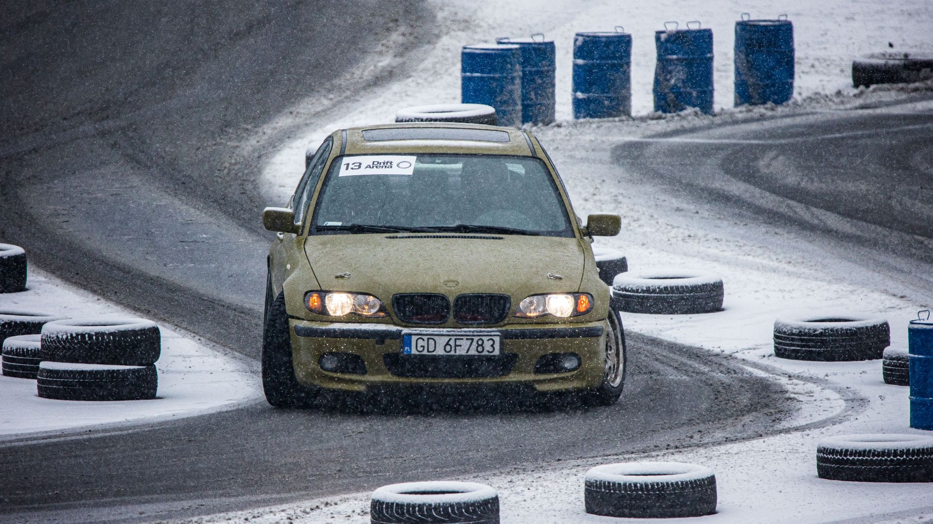 A BMW car expertly drifts on a snow-covered track, showcasing winter motorsport skills.