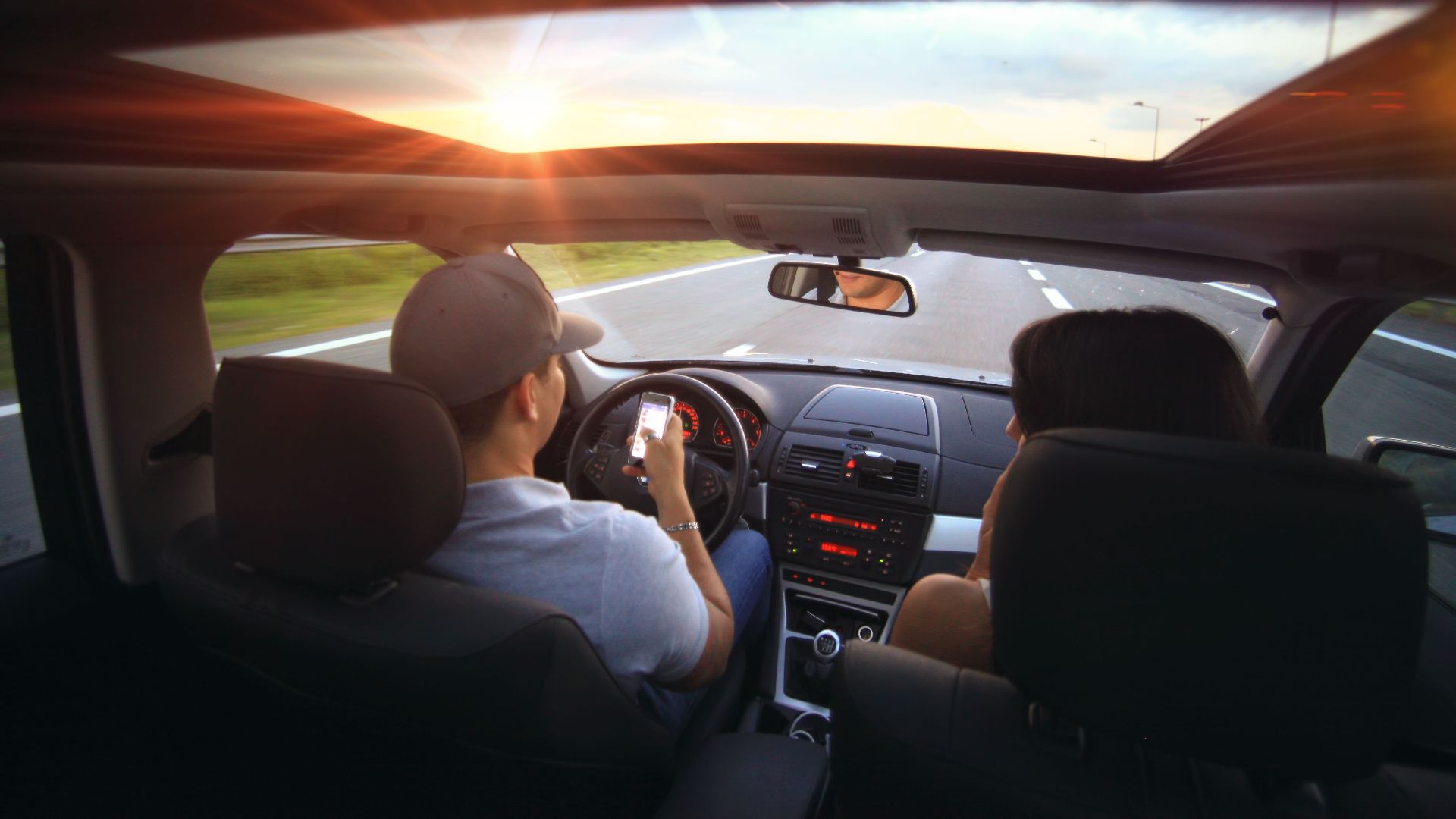 Driver using phone while driving at sunset with passenger in vehicle.