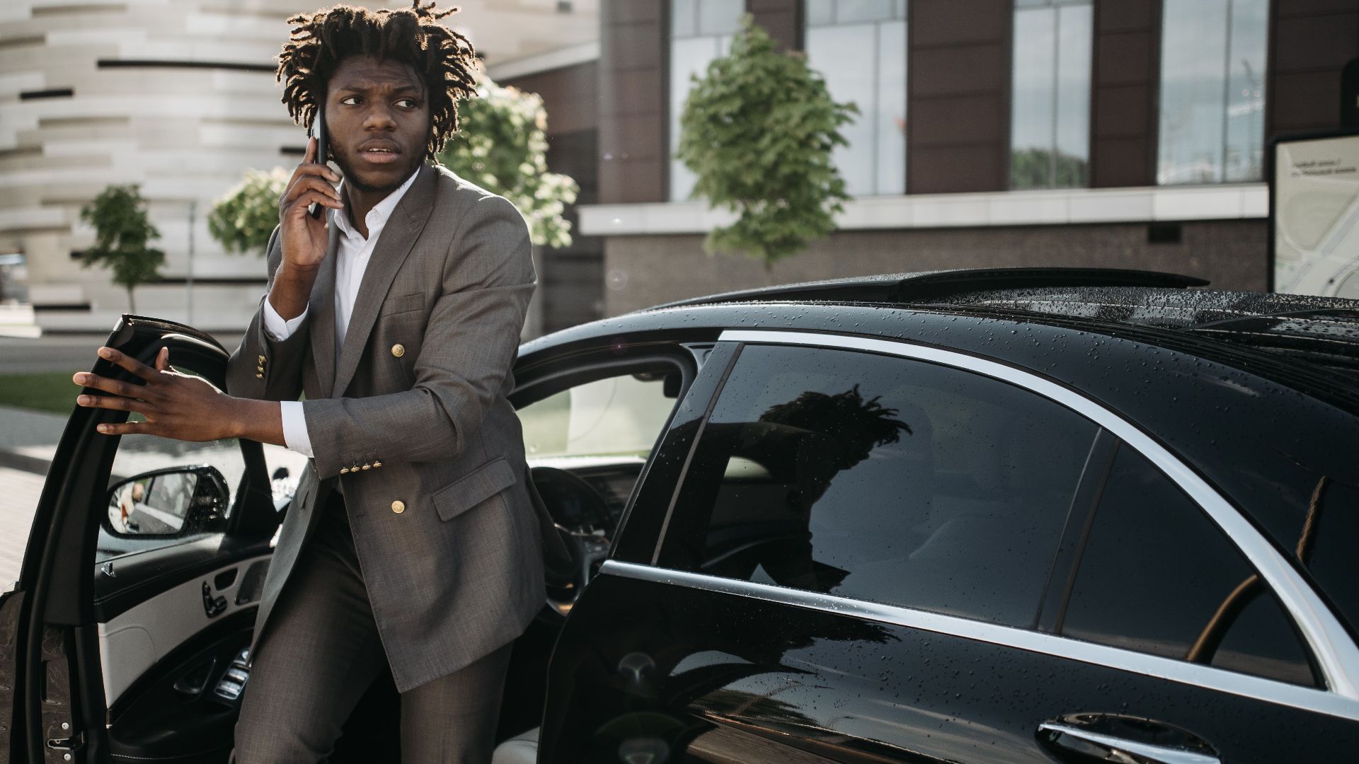 Confident businessman in a suit talking on a smartphone while getting out of a luxury black vehicle.