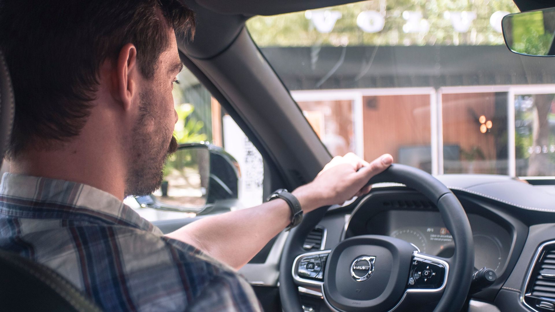 A man in casual attire is driving a modern car, focusing on the road.