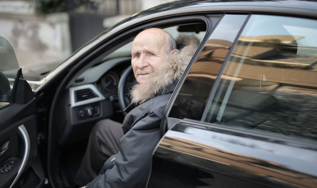 An elderly man in a winter coat stepping out of a parked car
