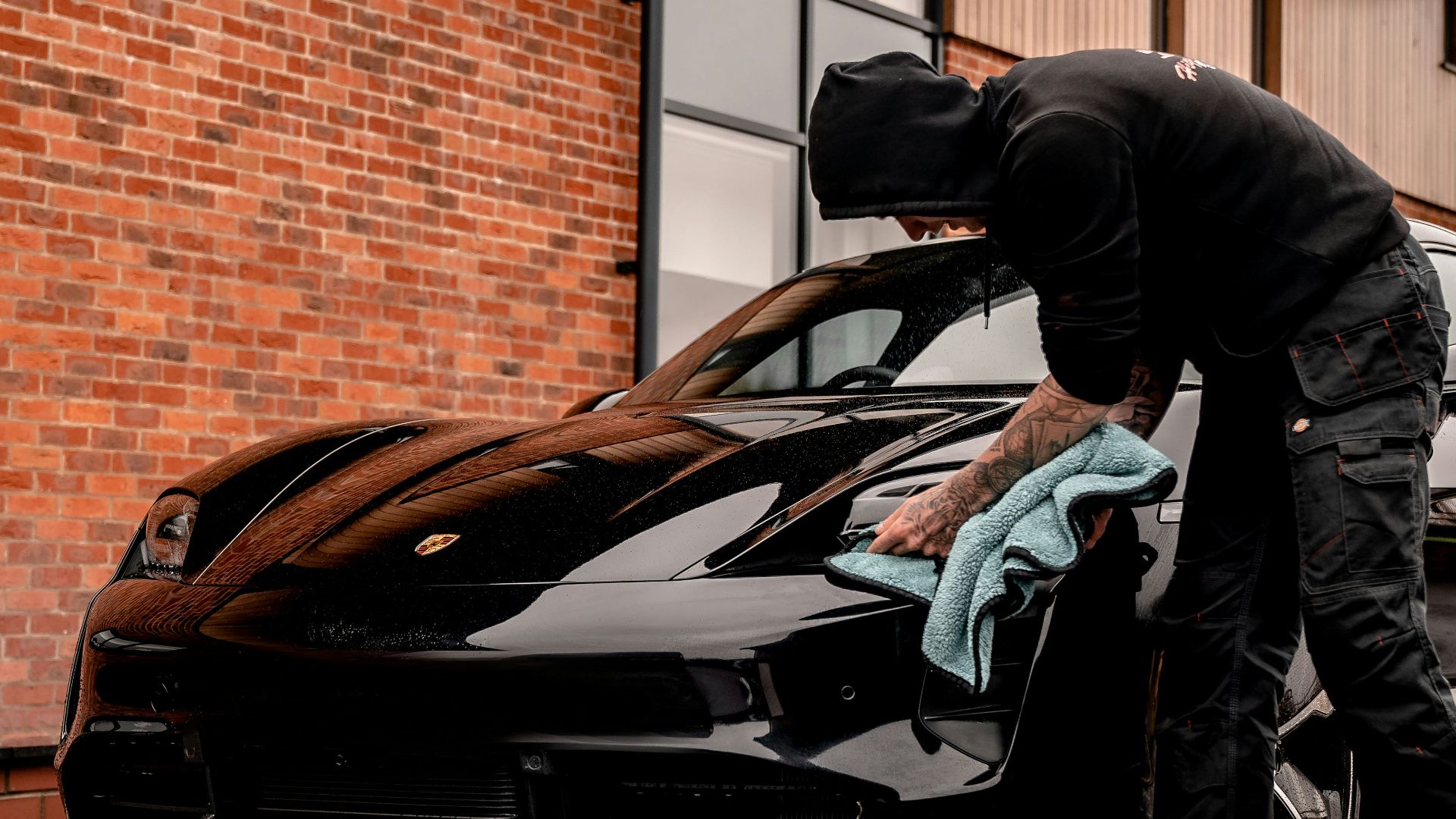 man in black jacket and blue denim jeans standing beside black bmw coupe