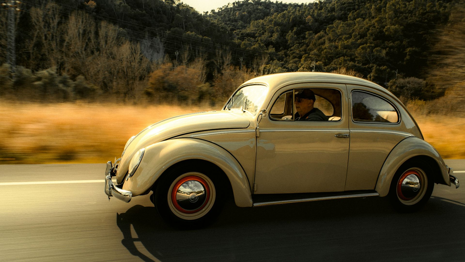 A vintage volkswagen beetle drives on a scenic road.