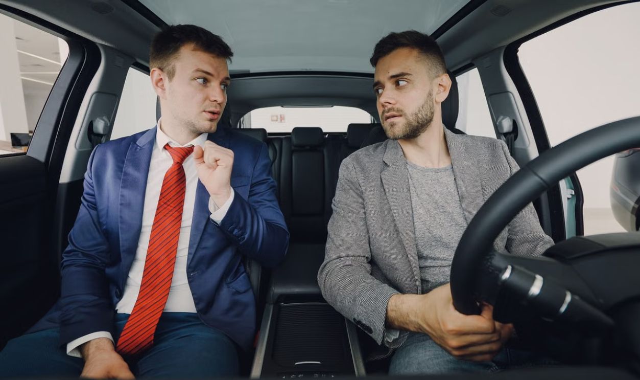 Two businessmen in a car engage in conversation, focusing on discussion details