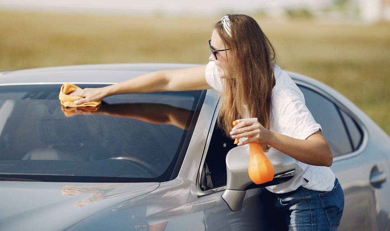 Young woman cleaning a car windshield with a cloth and spray bottle