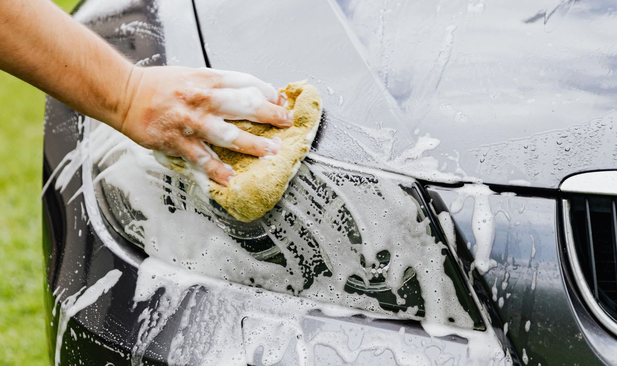 Person washing a black car's headlight with a sponge and soap