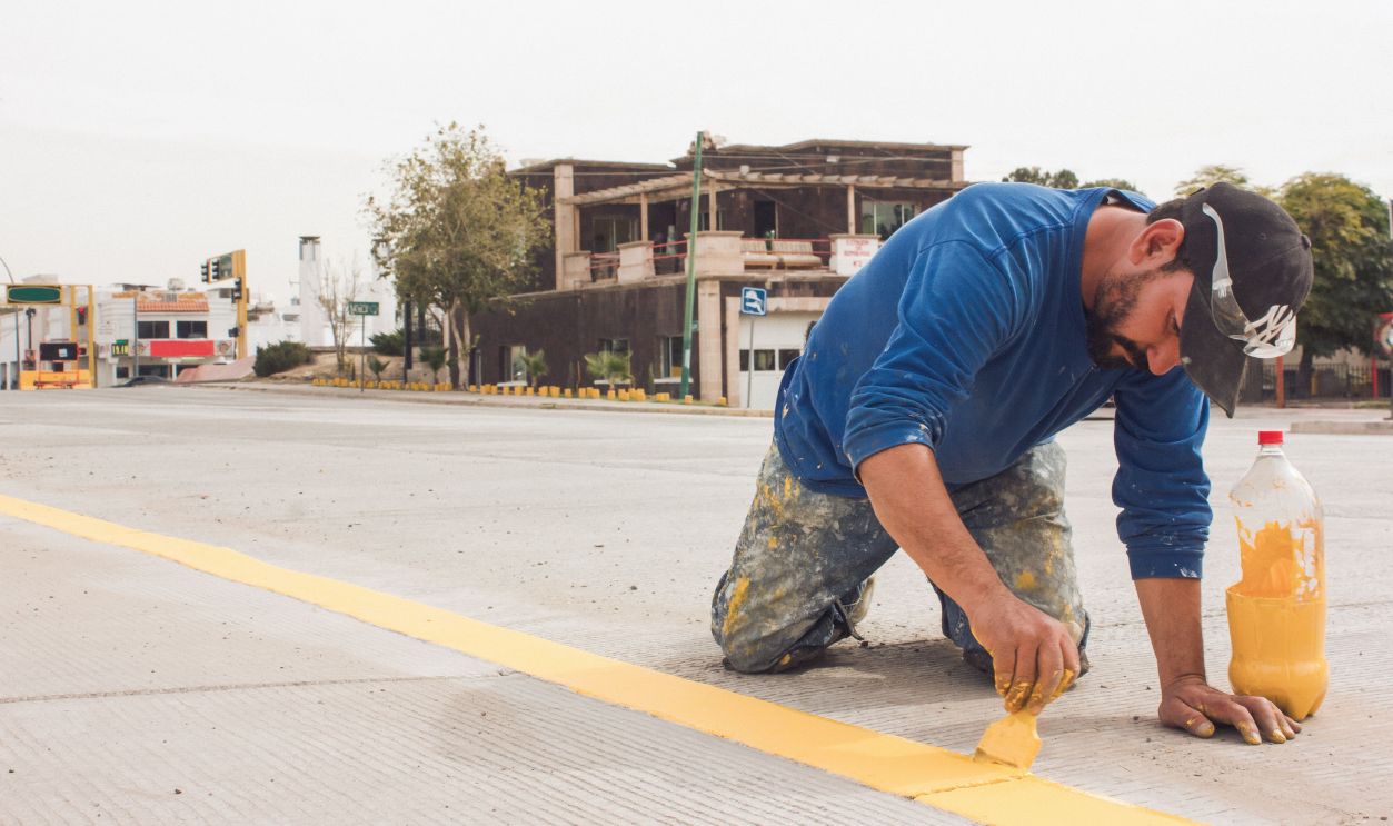 A man paints yellow road lines on an urban street, emphasizing urban infrastructure