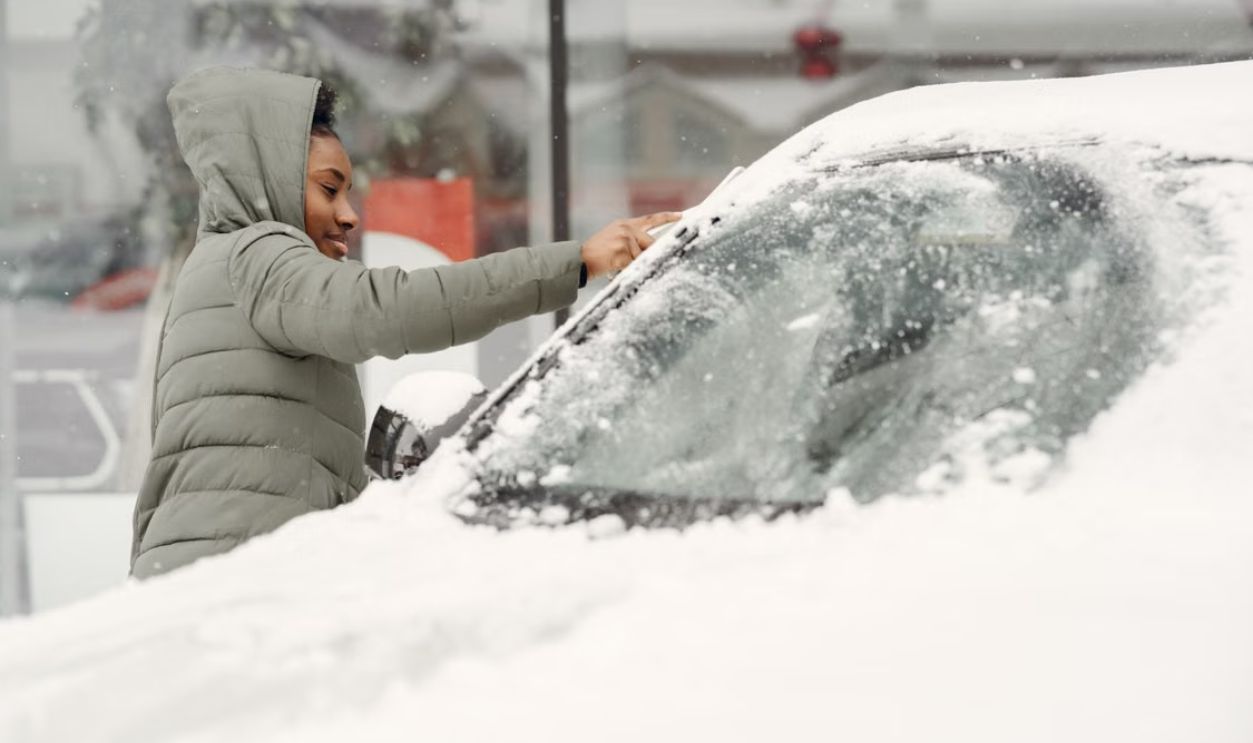 African American woman removing snow from car during a winter day outdoors.