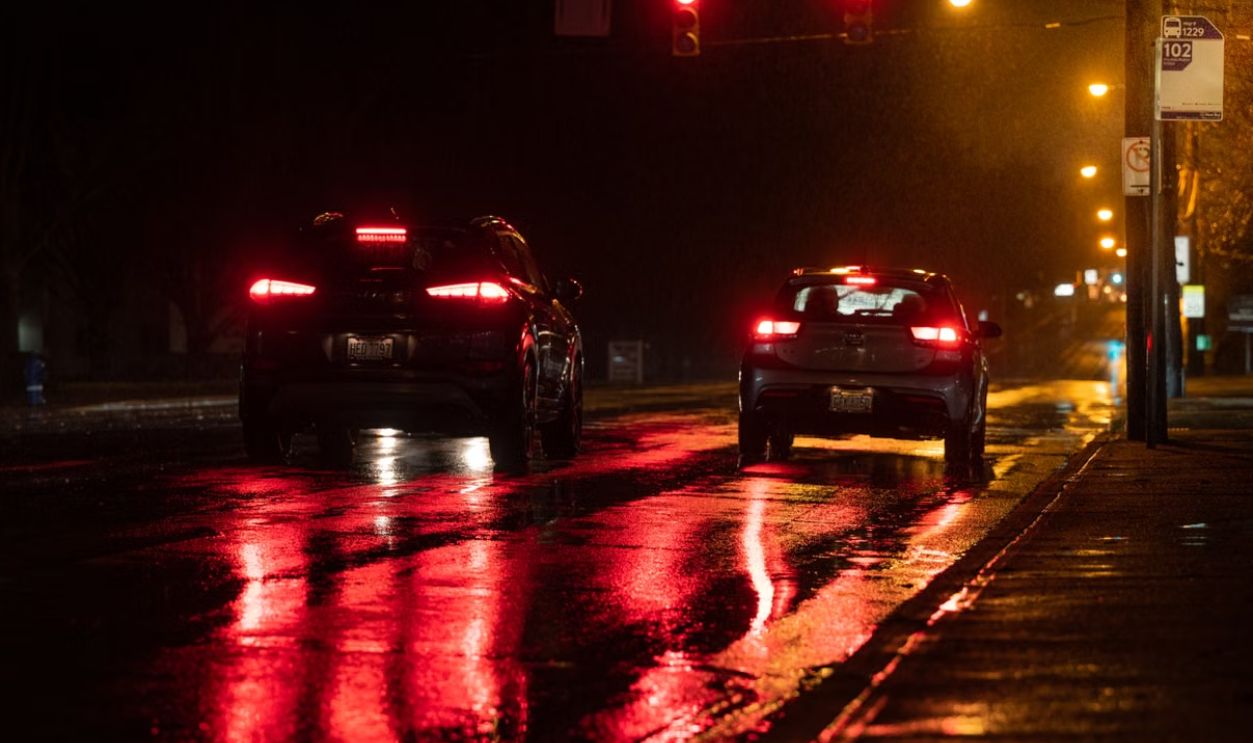 Nighttime scene of cars on a wet road showcasing red reflections from traffic lights.