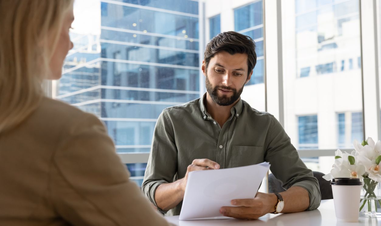 Professional business man attentively reads documents sits across table from woman in office, during formal business meeting or job interview, review data or resume paper. Human resources, staffing