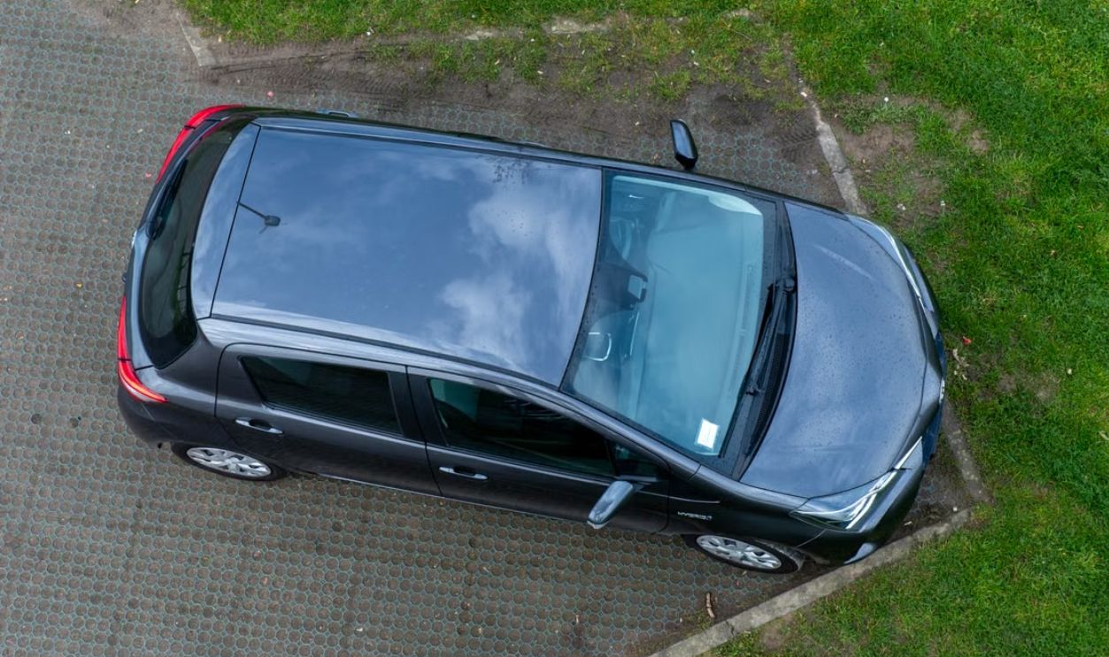 Top view of a black car parked on a grass and concrete surface, showcasing its exterior design