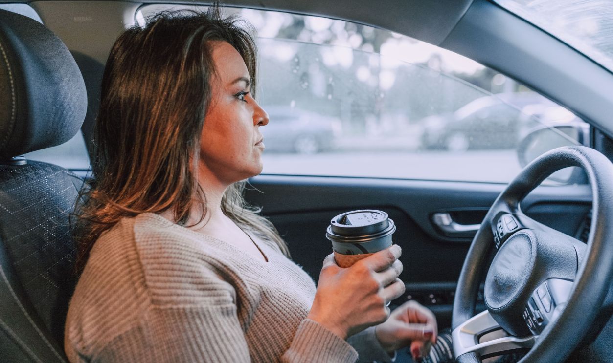 A woman in a car holding a disposable coffee cup