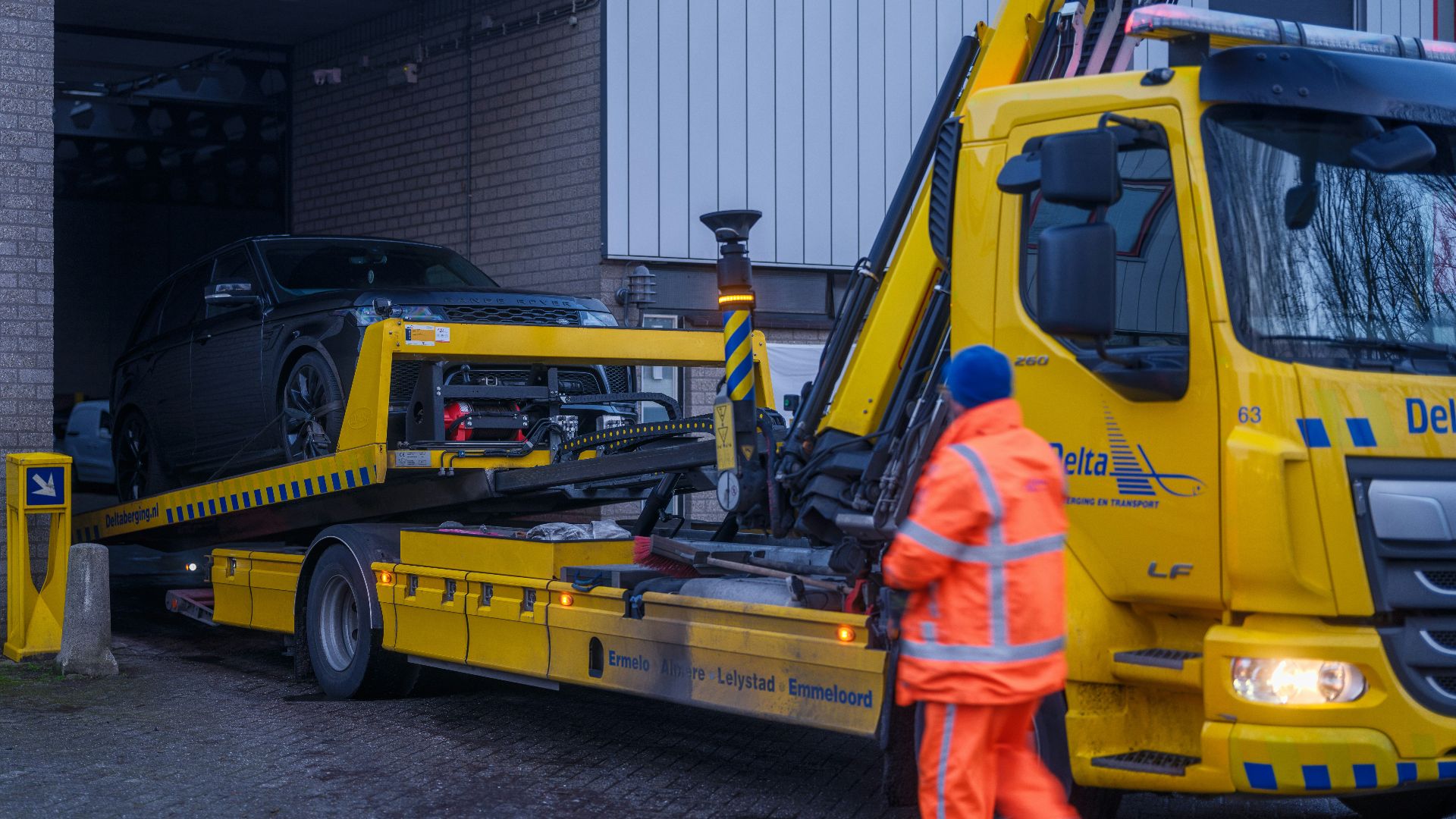A man in an orange safety suit standing next to a yellow tow truck