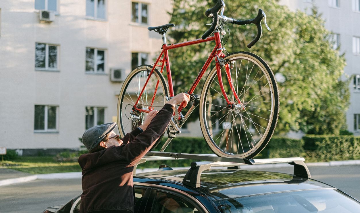 A man secures a red bicycle on top of a car's roof rack in an urban setting