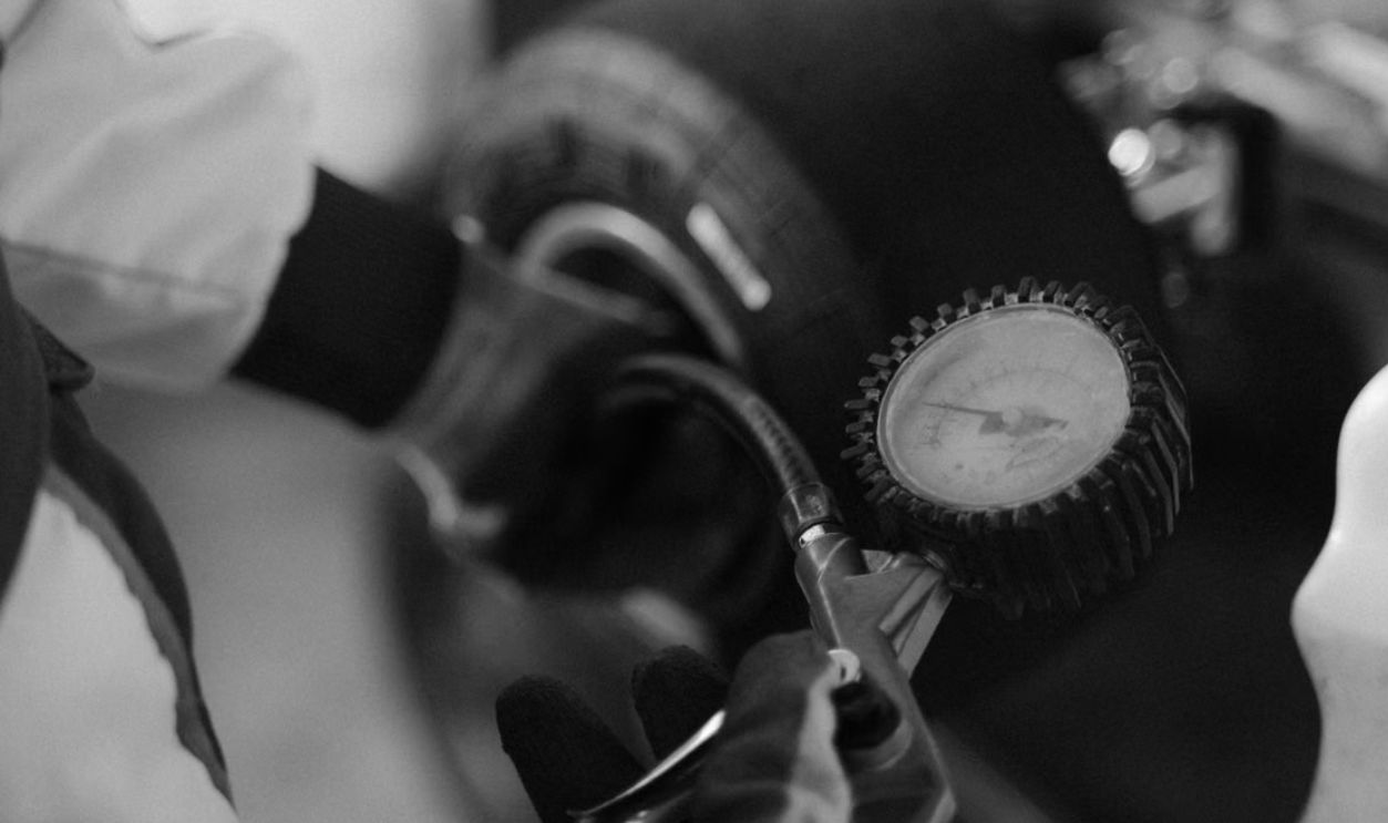 Black and white image of a mechanic using a gauge to check tire pressure on a kart wheel
