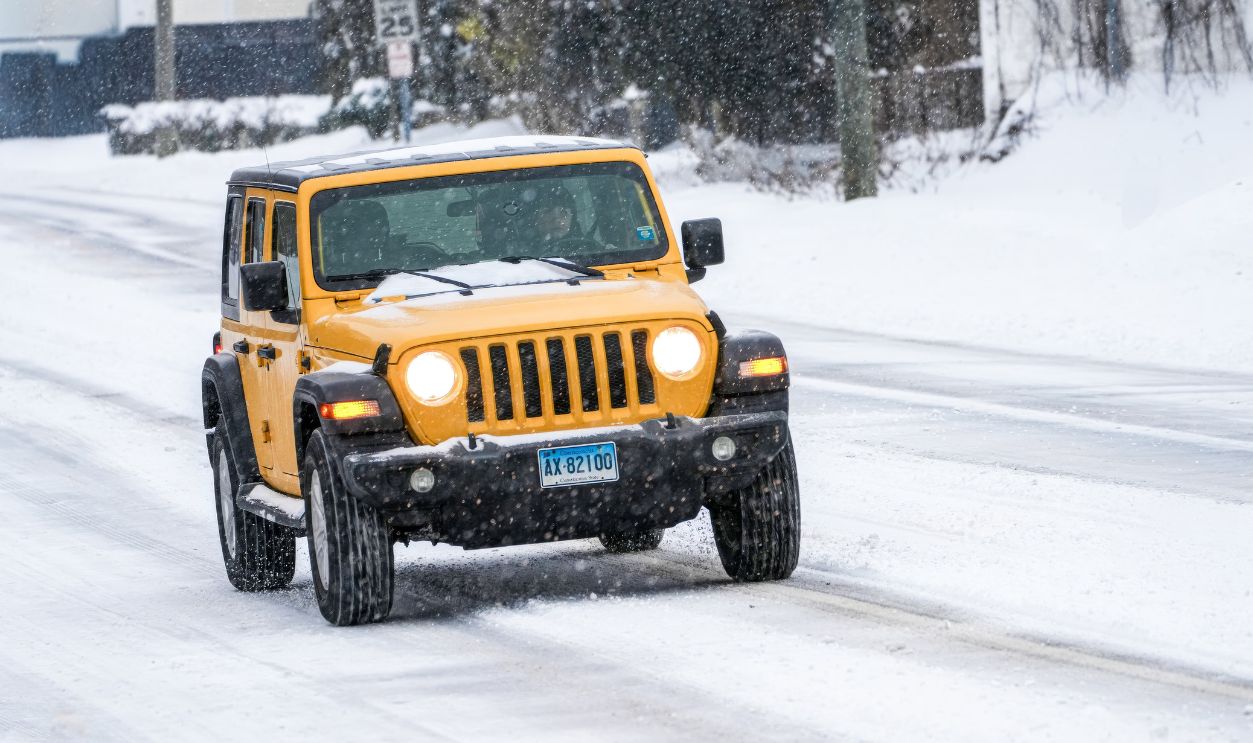 A vibrant yellow SUV navigates through a snowy urban street in winter conditions
