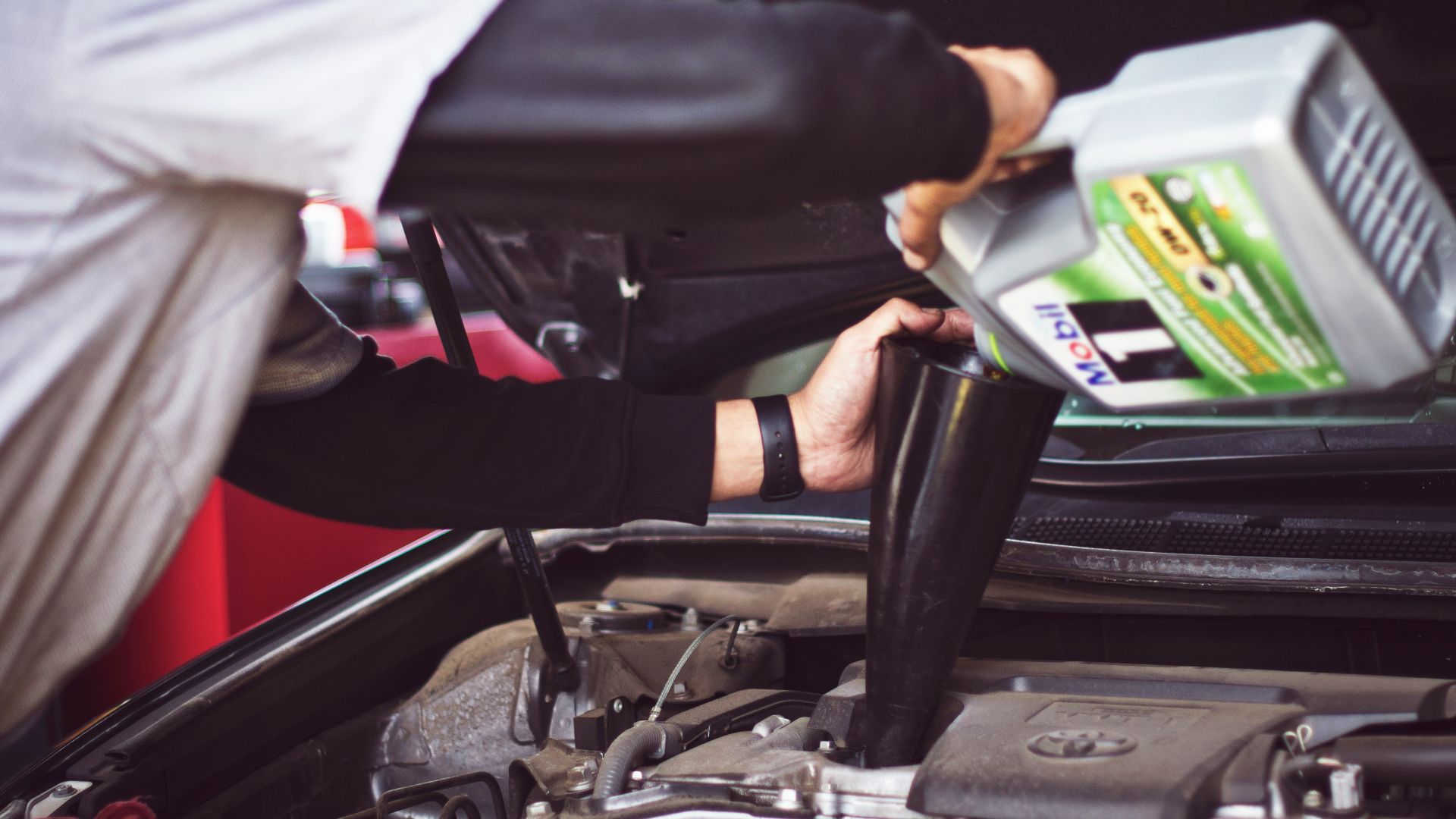 man refilling motor oil on car engine bay