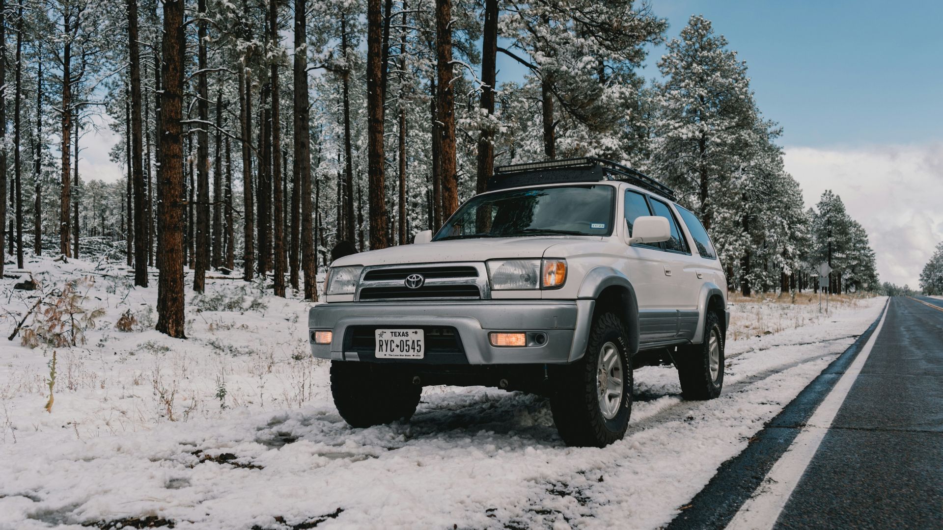 A silver truck driving down a snow covered road