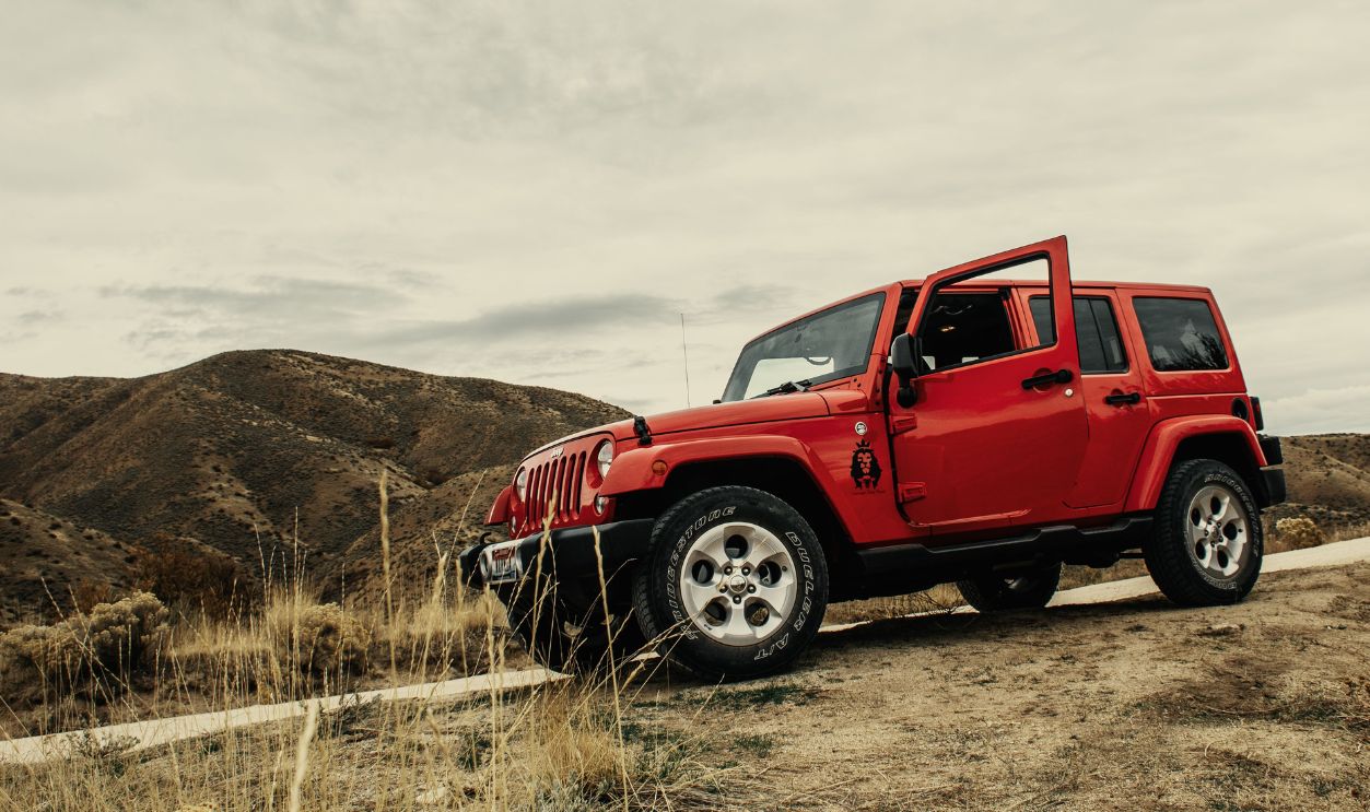 A vibrant red SUV parked on a dirt road with a mountain landscape backdrop under a cloudy sky