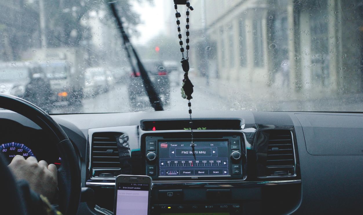 Car interior with driver navigating rainy cityscape using phone
