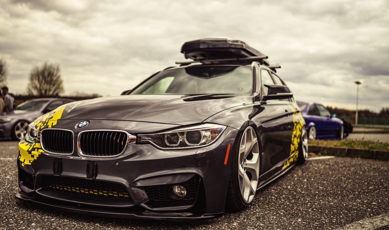A sleek, customized BMW F30 sedan with roof rack displayed outdoors