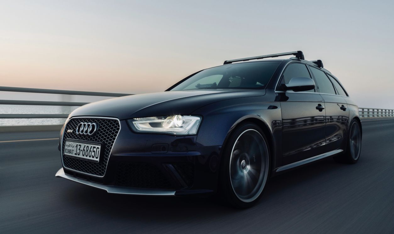 A sleek black Audi car drives on a highway during sunset, capturing elegance and speed.