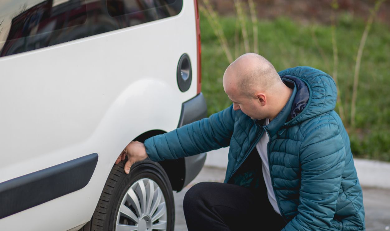 The man crouched beside the wheel of the car and touches checking or inflated