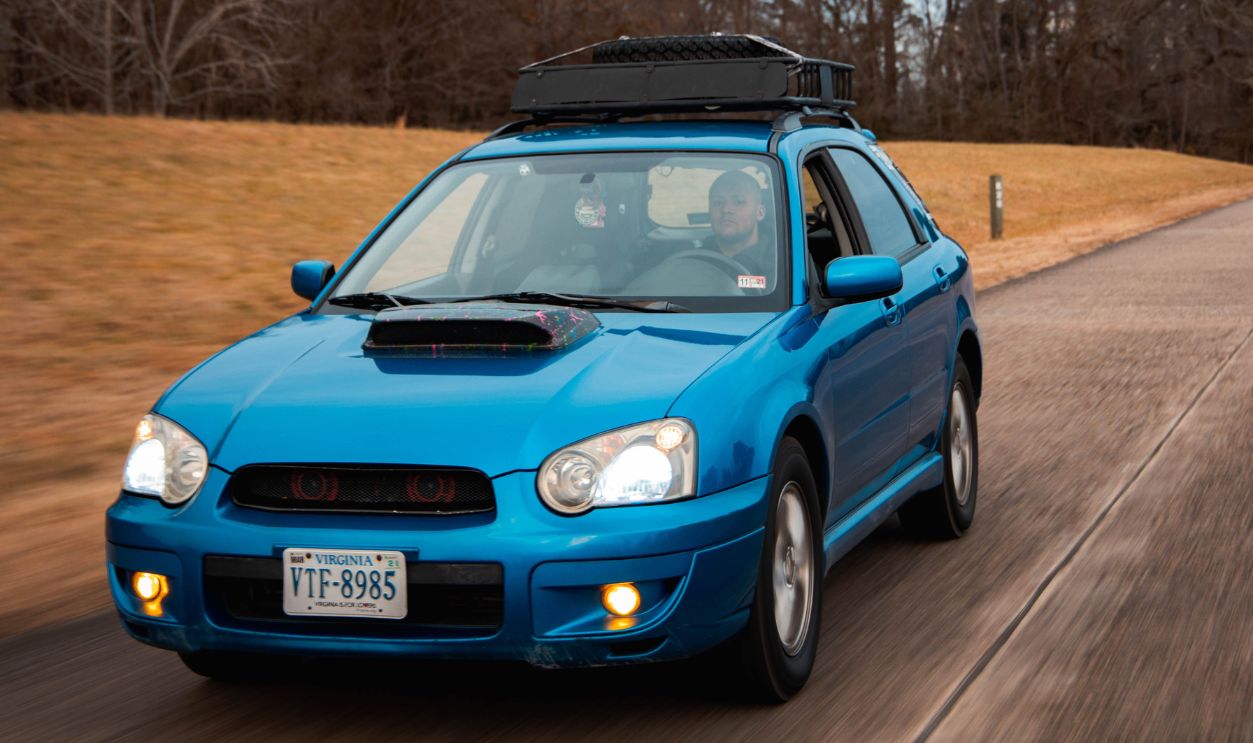 Blue Subaru car driving on a scenic rural road with trees in the background