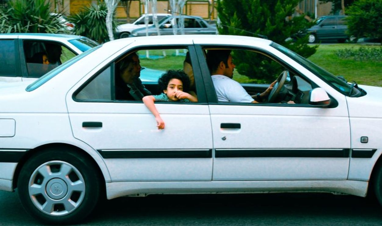 A family on a car ride, including a child looking out the window, in an urban setting.