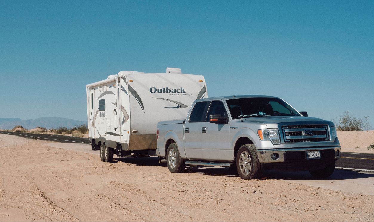 Silver truck towing an Outback trailer on a desert road