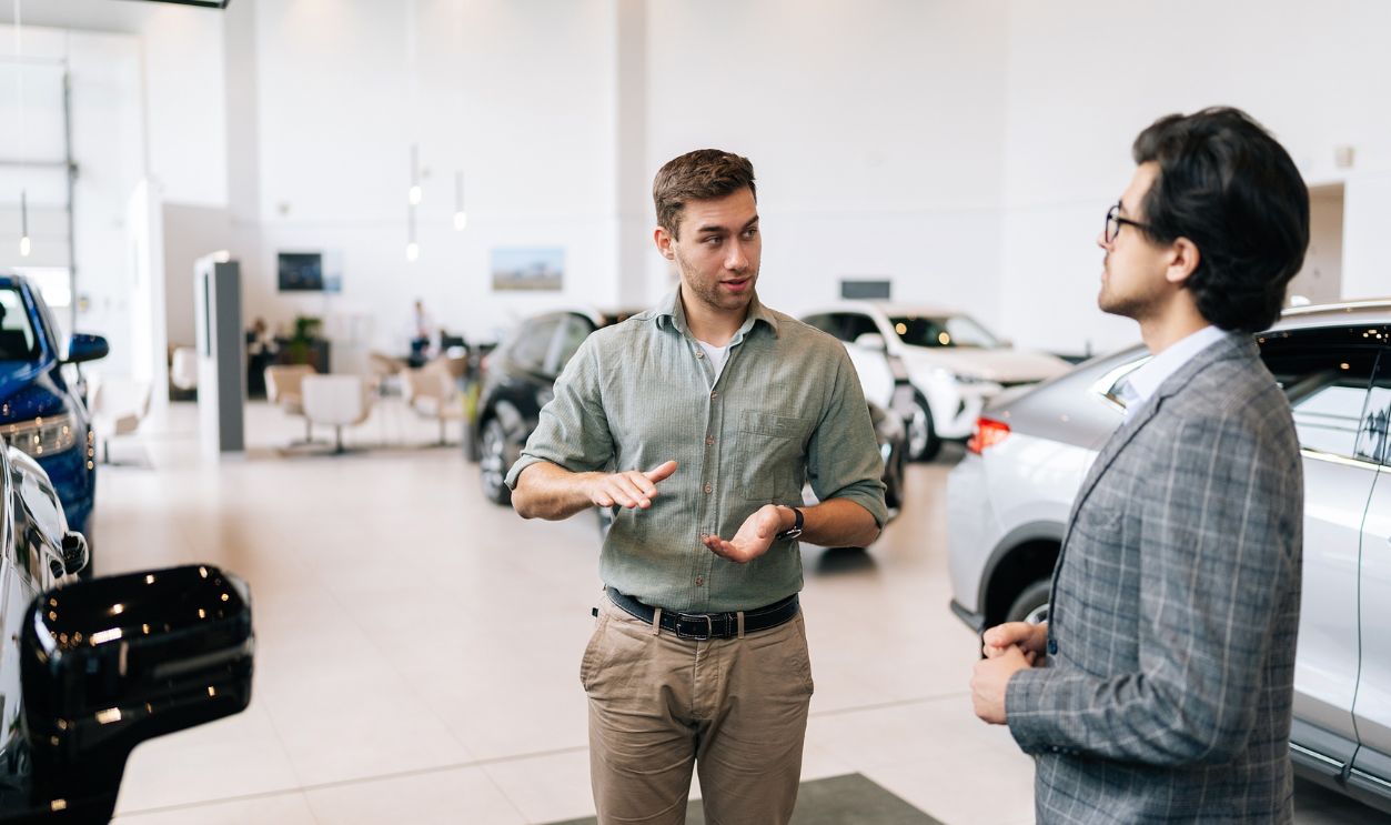 Portrait of serious male client talking to professional car dealer in business suit in dealership discussing automobiles looking at luxurious new model. Concept of choosing and buying new auto.