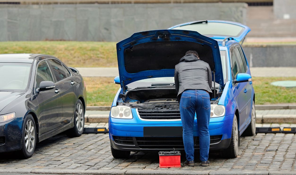 Man changing car battery under open hood during cold winter weather, vehicle breakdown, emergency roadside repair. Winter car maintenance, man replacing dead battery after cold start failure
