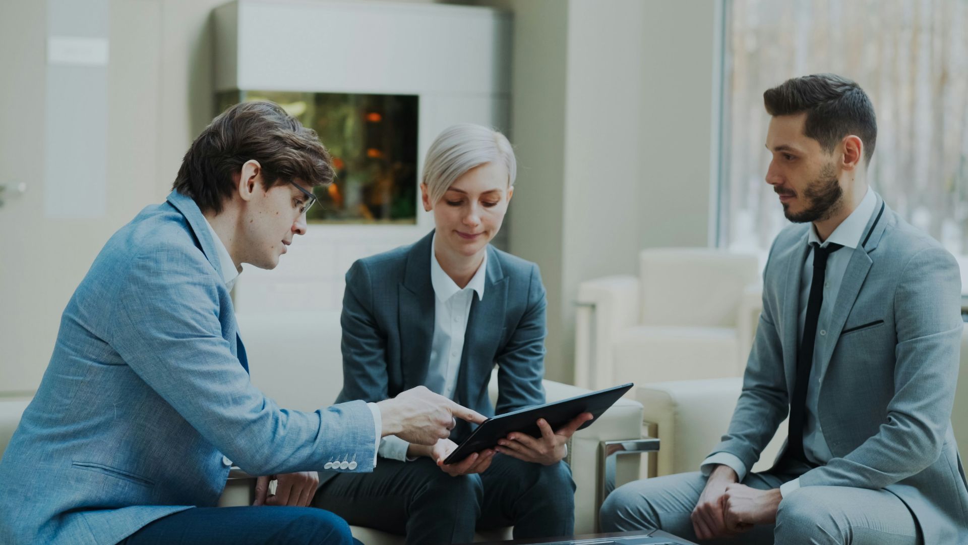 Three professionals discussing a tablet in a modern office.
