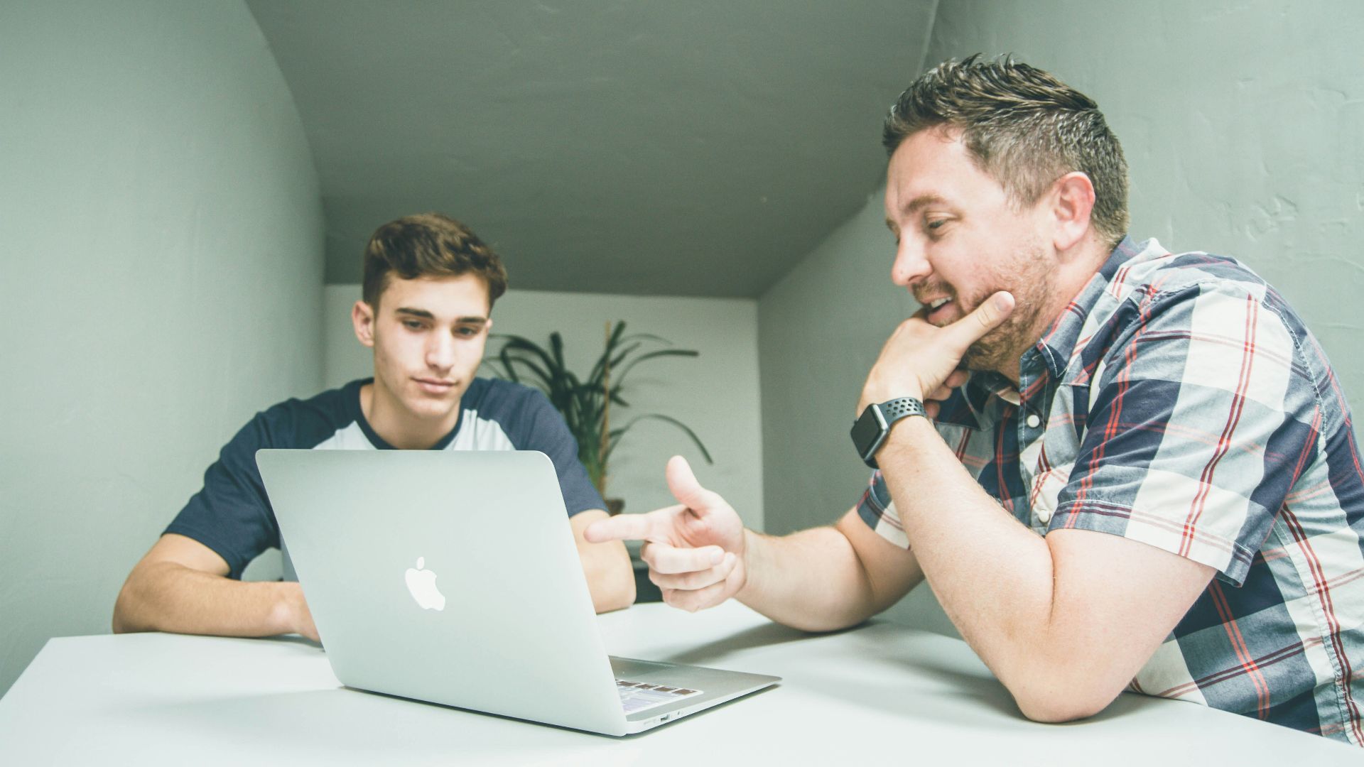 man wearing white and black plaid button-up sports shirt pointing the silver MacBook