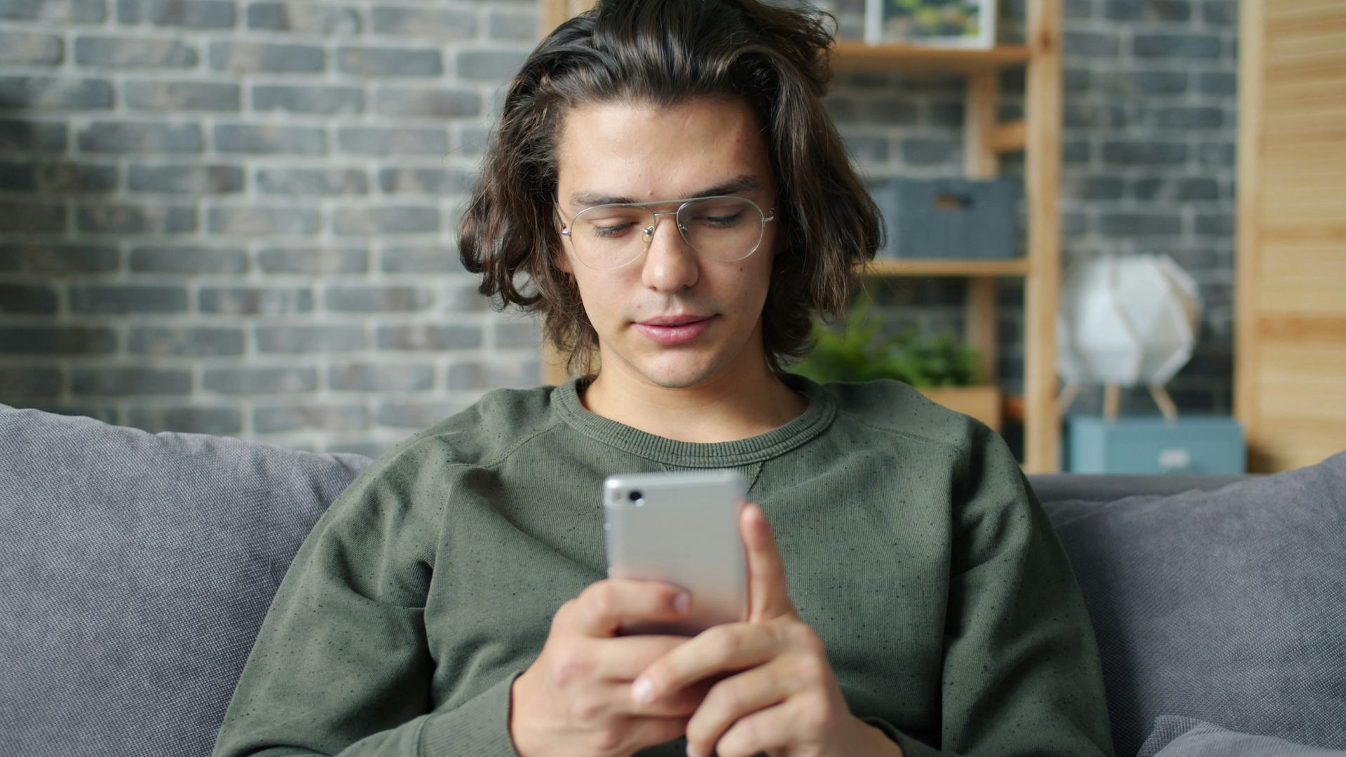 Young man with glasses using a smartphone on couch.