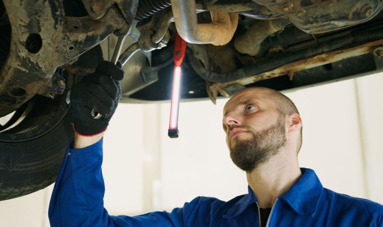 Mechanic focusing on vehicle maintenance under a car lift in a garage