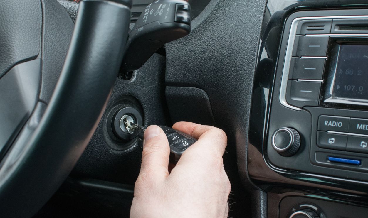 The male driver's hand inserting the key into the ignition lock of the car, on the background of the steering wheel and panel