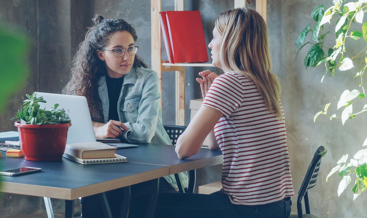 Two women are sitting at a desk in office 