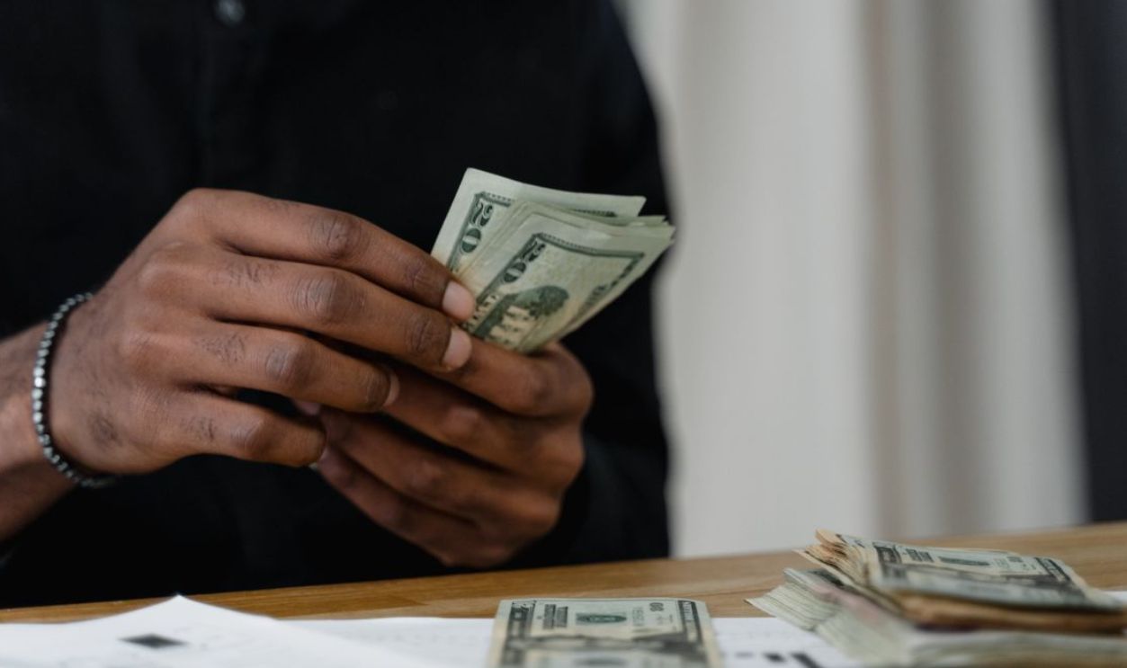Adult counting dollar bills at a desk, focused on money management and finance