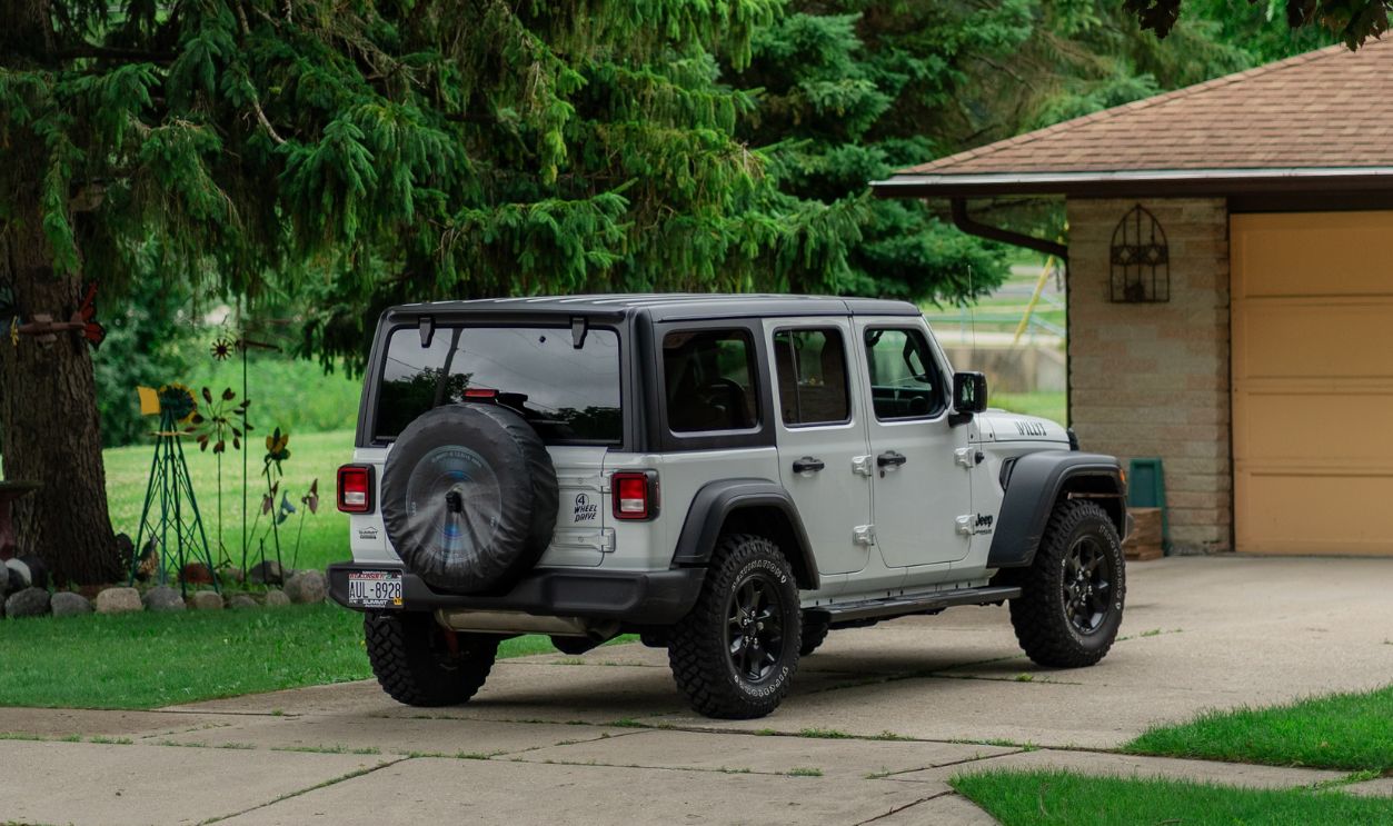 A silver SUV is parked in a suburban driveway surrounded by green trees and grass
