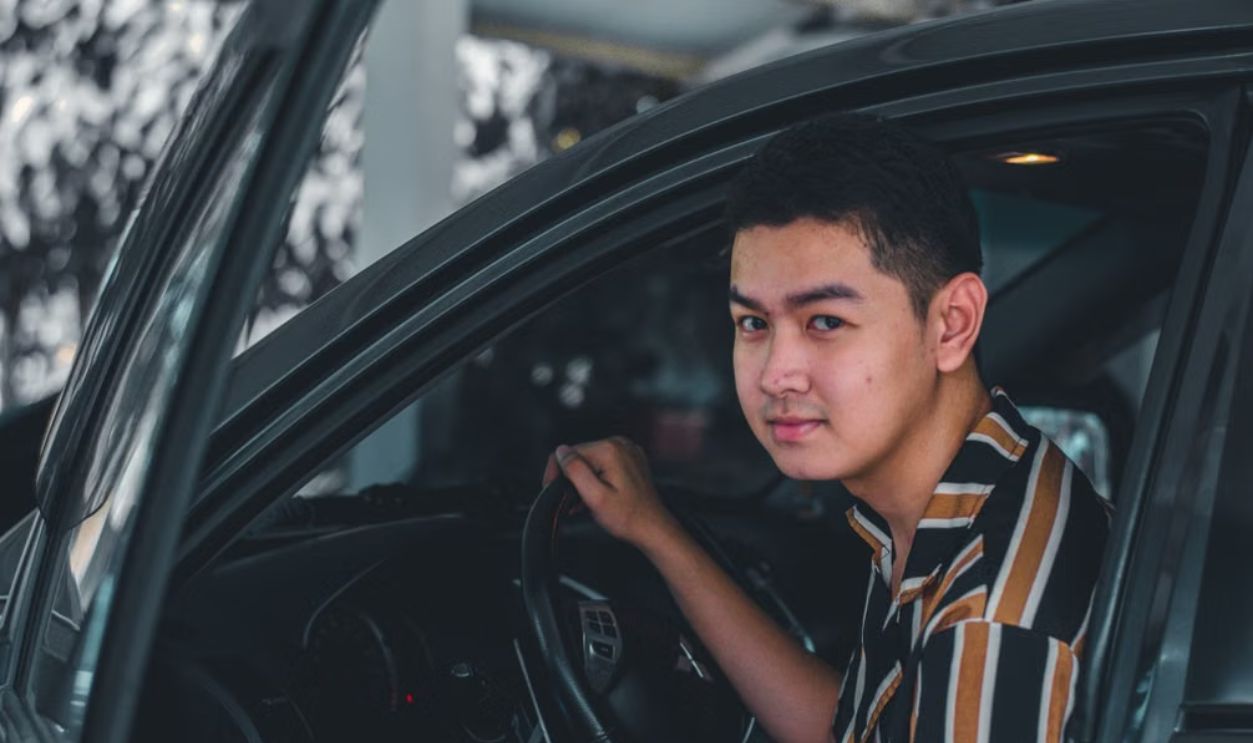 A young man smiling while sitting in a car, captured outdoors. Perfect for themes of travel and lifestyle