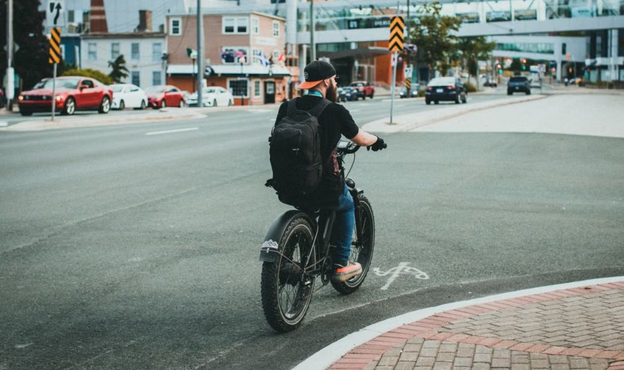 Man riding a bicycle on a city street while wearing a backpack, urban life