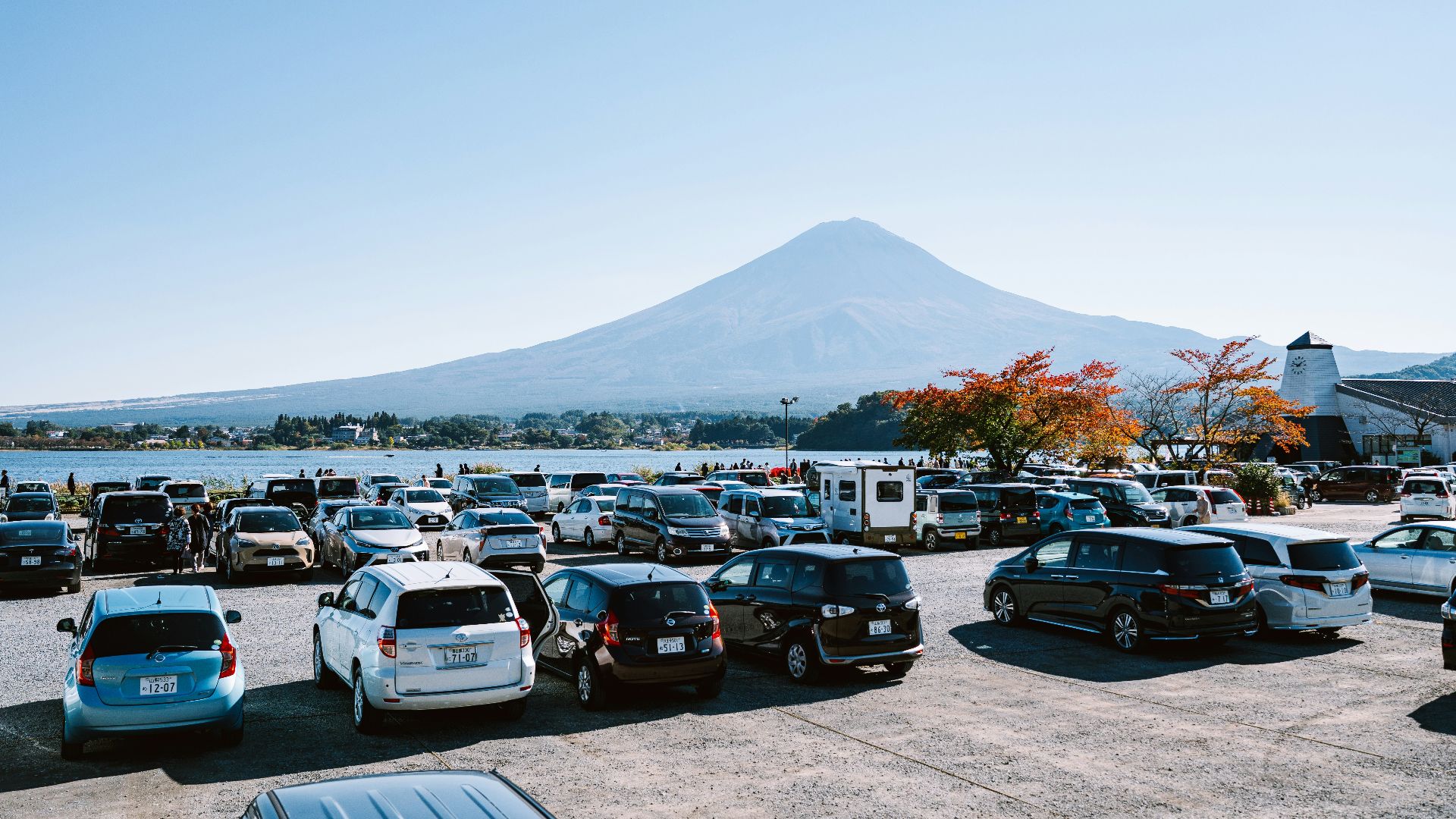 Mount fuji overlooks a crowded parking lot near a lake.
